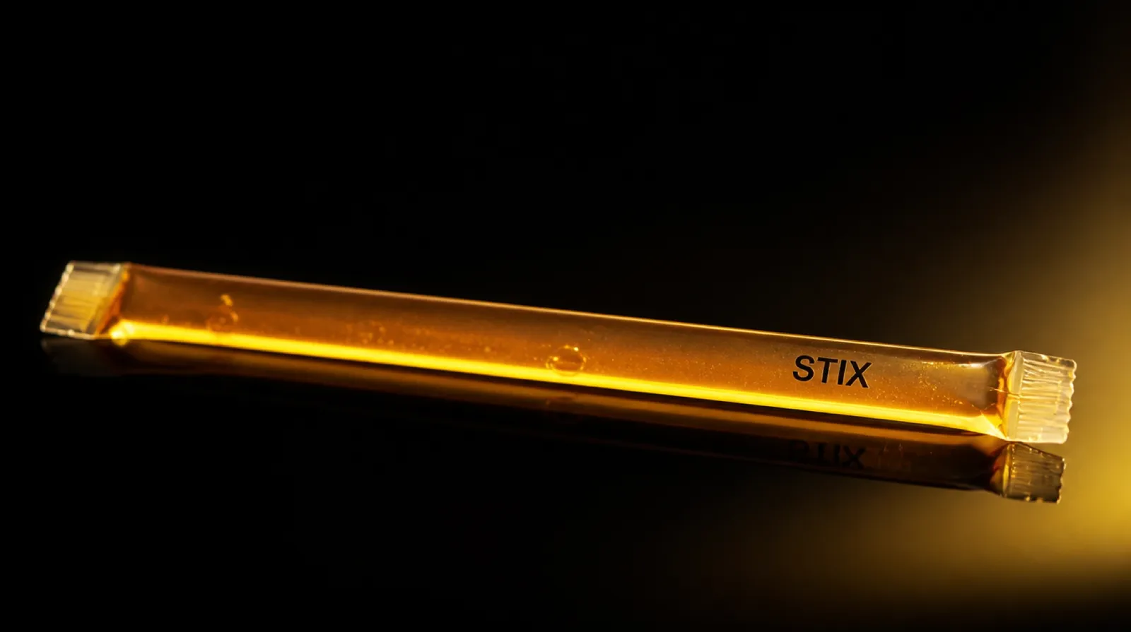 A single thin translucent amber Stix honey straw, both ends heat-sealed, honey glowing through the wall